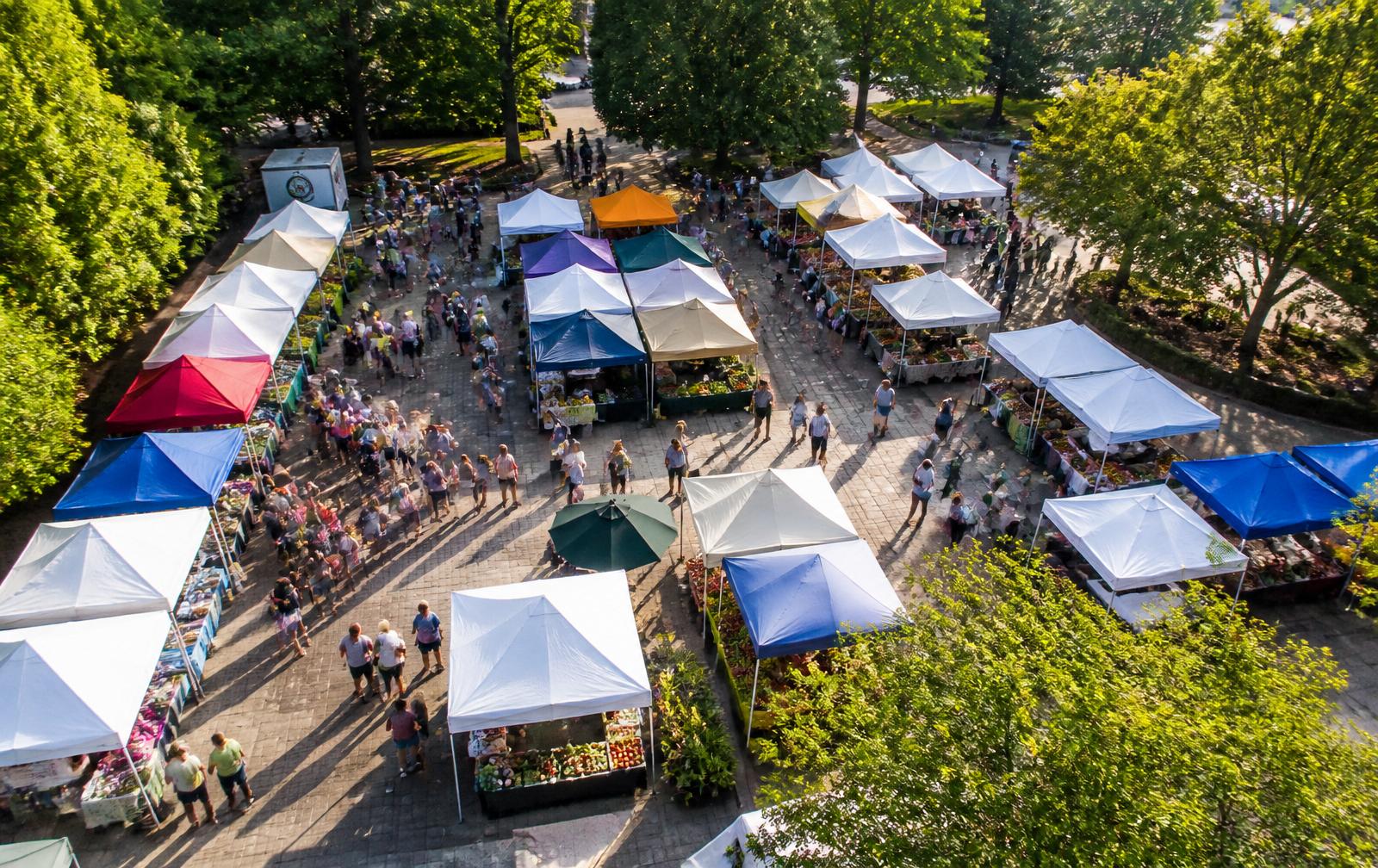 Aerial drone view of a vibrant outdoor farmers market with colorful vendor tents and shoppers